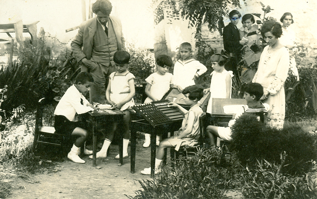 Α' τάξη Προτύπου, Ιούνιος 1928. Ομάδα παιδιών του Προτύπου εργάζεται στο ύπαιθρο. Ο Μίλτος Κουντουράς, η Αλεξάνδρα Κεσσανλή και τελειόφοιτες του Διδασκαλείου παρακολουθούν την εργασία των παιδιών.
